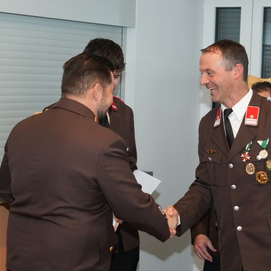 Zwei Männer in Militäruniformen schütteln sich die Hände, lächeln und befinden sich möglicherweise in einem formellen Rahmen.