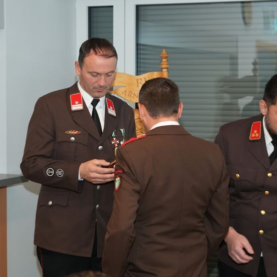 Ein Militäroffizier befestigt eine Medaille an der Uniform eines anderen Offiziers in einer formellen Umgebung.