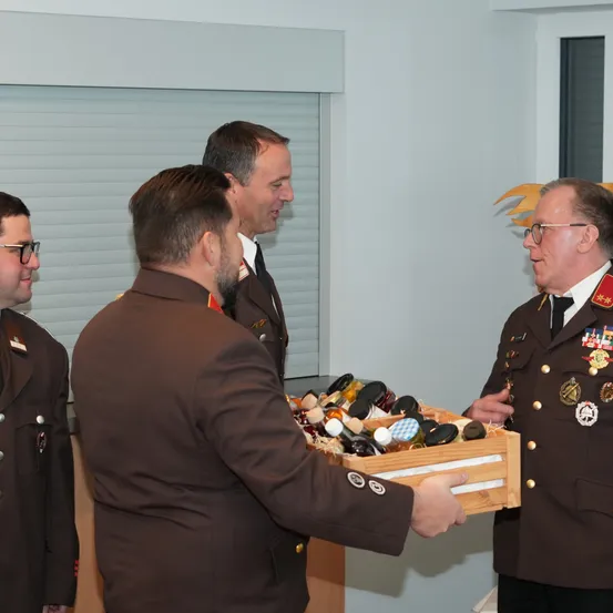 Vier Männer in Militäruniformen stehen in einem Raum mit einem Fenster. Ein Mann hält eine Schachtel mit verschiedenen Flaschen.