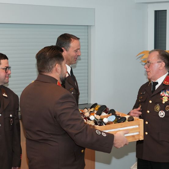 Vier Männer in Militäruniformen stehen in einem Raum mit einem Fenster. Ein Mann hält eine Schachtel mit verschiedenen Flaschen.