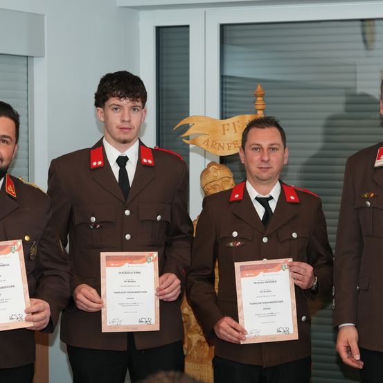 Vier Männer in Militäruniformen stehen nebeneinander und halten Urkunden. Sie sind wahrscheinlich Militärangehörige, die Auszeichnungen erhalten.