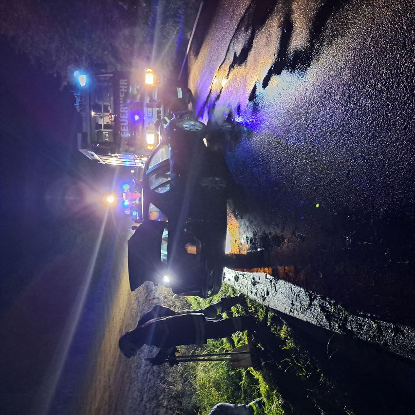 Ein Rettungsfahrzeug steht nachts auf der nassen Straßenseite. Eine Person in einer reflektierenden Weste steht neben dem Fahrzeug.