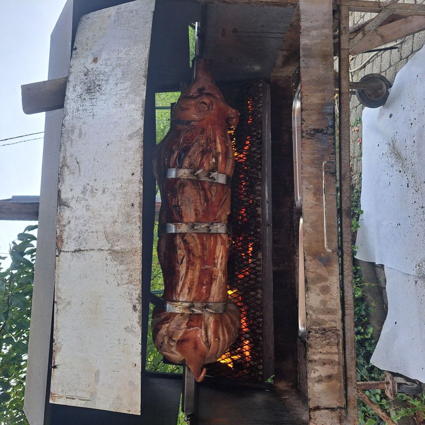 Ein ganzes gebratenes Schwein wird in einem großen Metallgrill gekocht, gesichert mit Metallbändern. Der Grill ist offen und zeigt Flammen darunter.