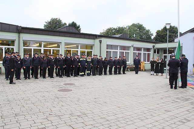 Eine Gruppe uniformierter Personen steht vor einem Gebäude, einige vor einem Fahnenmast.