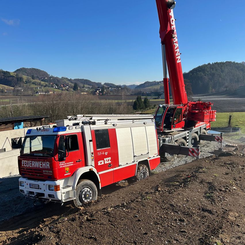 Ein roter und weißer Feuerwehrwagen mit einem Kran steht auf einem Feldweg. Der Kran ist am Wagen befestigt.