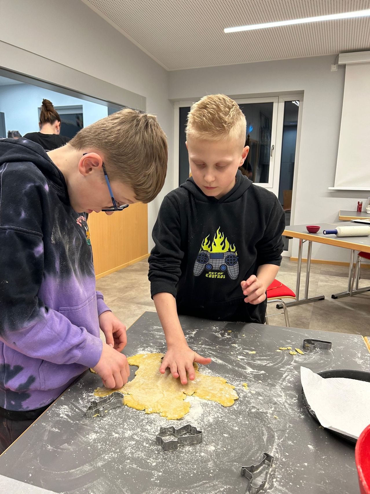 Zwei Jungen sind in einem Klassenzimmer und formen Kekse mit Ausstechern auf einem Tisch.