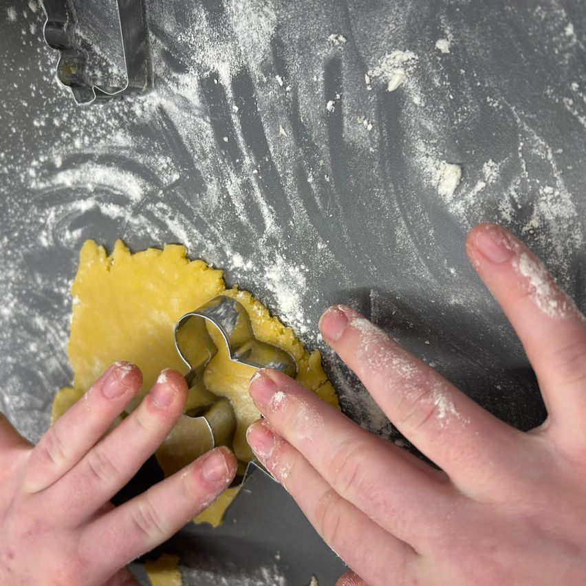 Zwei Hände verwenden einen Ausstecher, um in gelben Teig auf einer bemehlten Oberfläche zu schneiden.