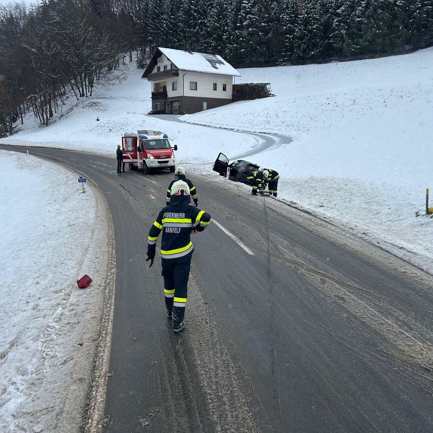 Rettungskräfte kümmern sich um einen Autounfall auf einer verschneiten Straße, ein Feuerwehrwagen steht in der Nähe.