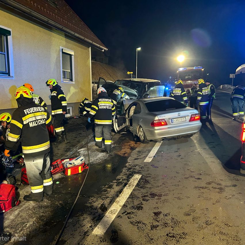 Einsatzkräfte kümmern sich um einen Unfall mit zwei Autos, von denen eines beschädigt ist, auf einer Straße bei Nacht.