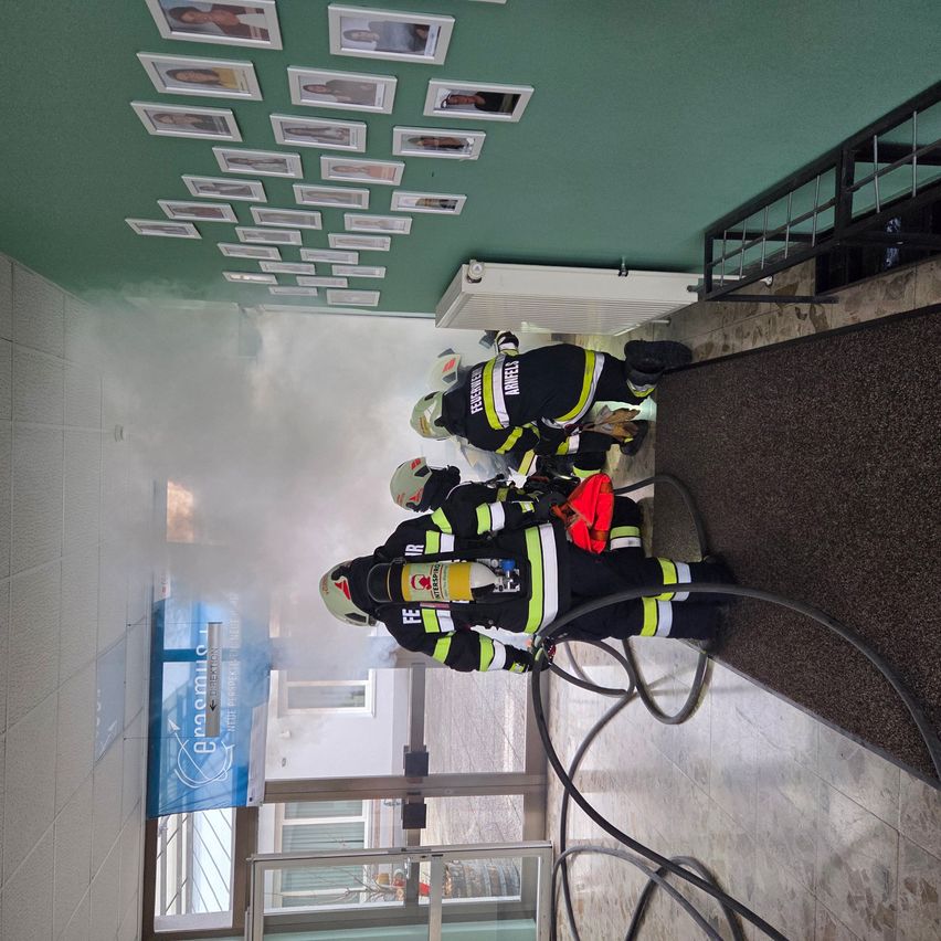 Eine Gruppe Feuerwehrleute arbeitet in einem rauchgefüllten Flur und verwendet Schläuche und Schutzausrüstung.