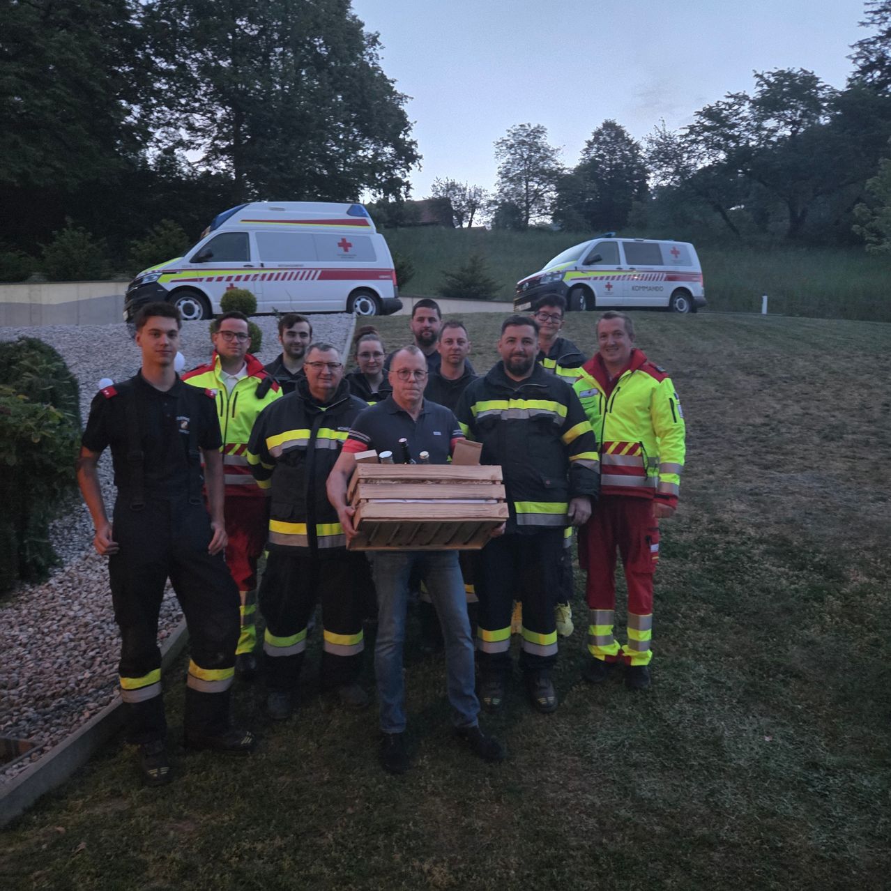 A group of emergency responders poses for a photo with a box, two ambulances in the background.