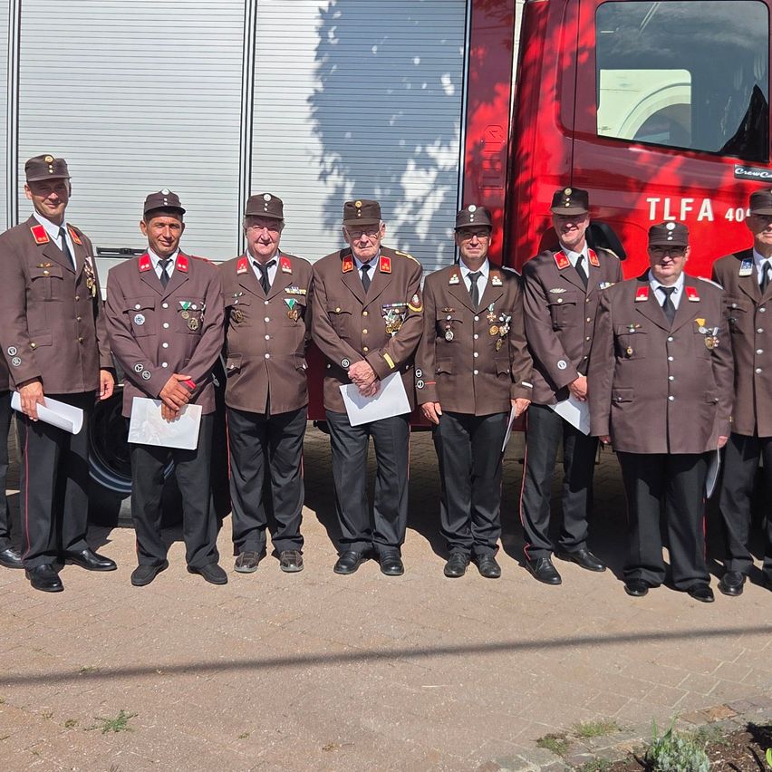 Eine Gruppe von Männern in braunen Uniformen mit Medaillen steht vor einem roten LKW.