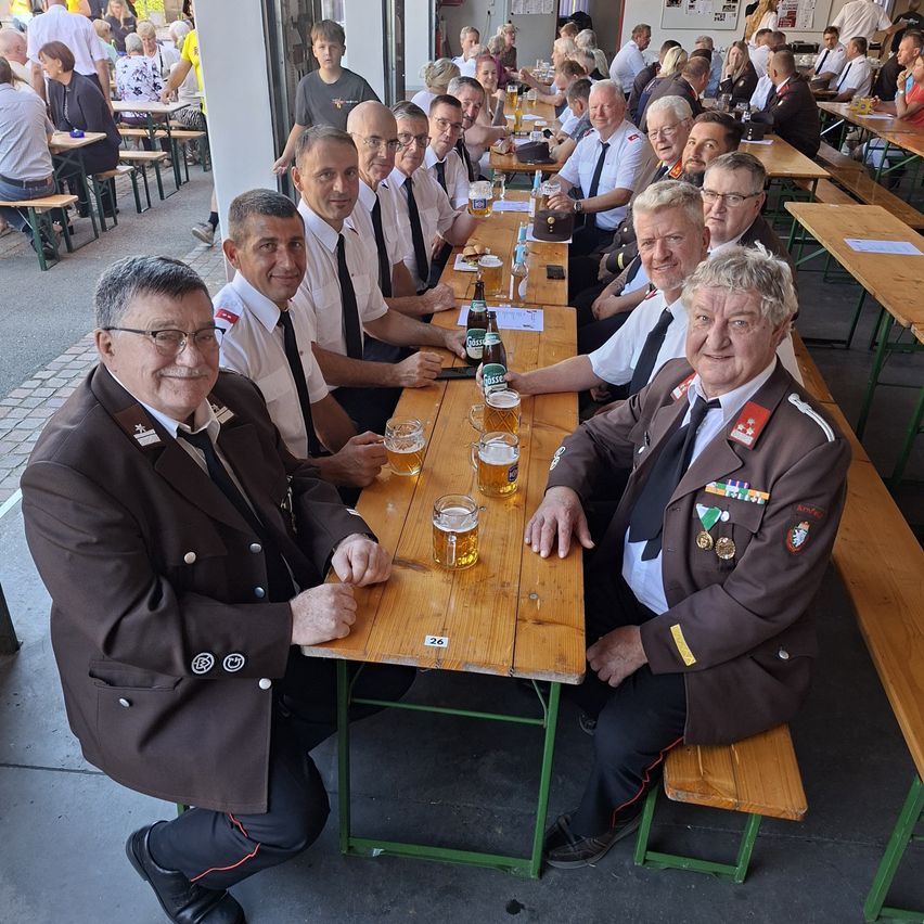 Eine Gruppe von Männern in Uniformen, möglicherweise Militär, sitzt an einem Tisch in einem Restaurant, lächelt und posiert für ein Foto. Sie haben Gläser Bier und Flaschen auf dem Tisch.