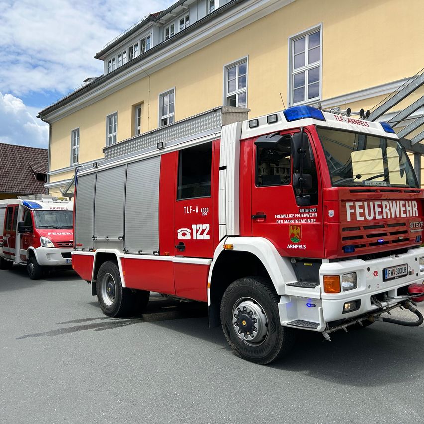 Ein Feuerwehrwagen mit der Nummer 122 steht vor einem gelben Gebäude mit mehreren Fenstern. Ein weiterer Feuerwehrwagen ist ebenfalls in der Nähe geparkt.