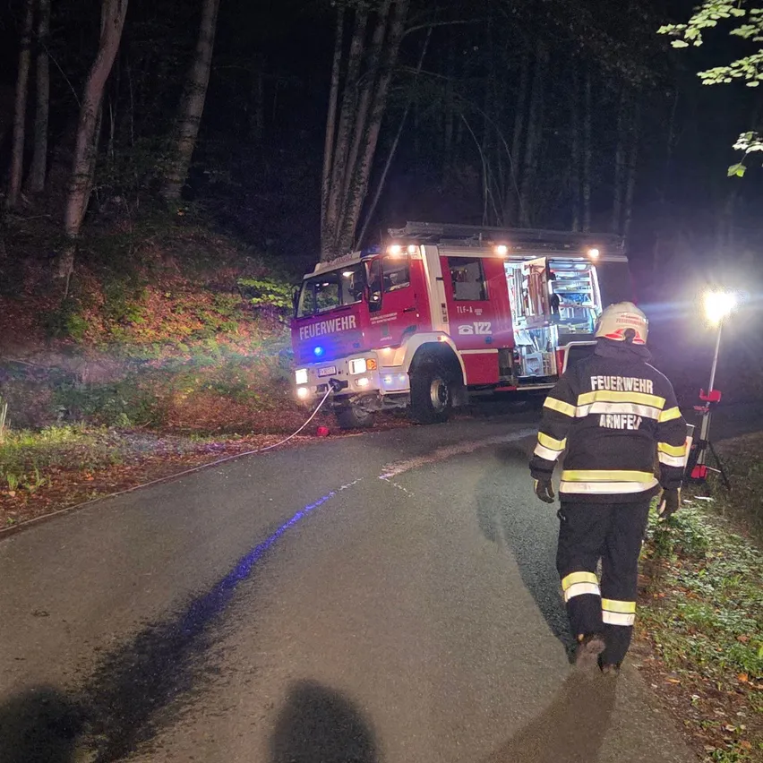 Ein Feuerwehrmann geht nachts auf einer dunklen Straße, ein Feuerwehrwagen ist in der Nähe geparkt.