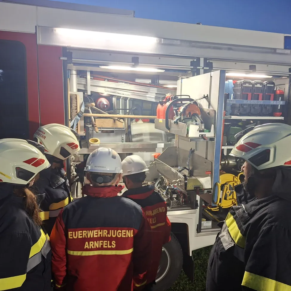 Eine Gruppe von Feuerwehrleuten steht um einen Feuerwehrwagen herum und schaut sich die Ausrüstung im Inneren an.