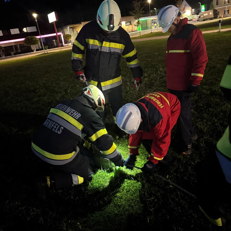 Fünf Feuerwehrleute in voller Ausrüstung sind auf einem Rasenfeld bei Nacht. Sie arbeiten an einem grünen Licht auf dem Boden.