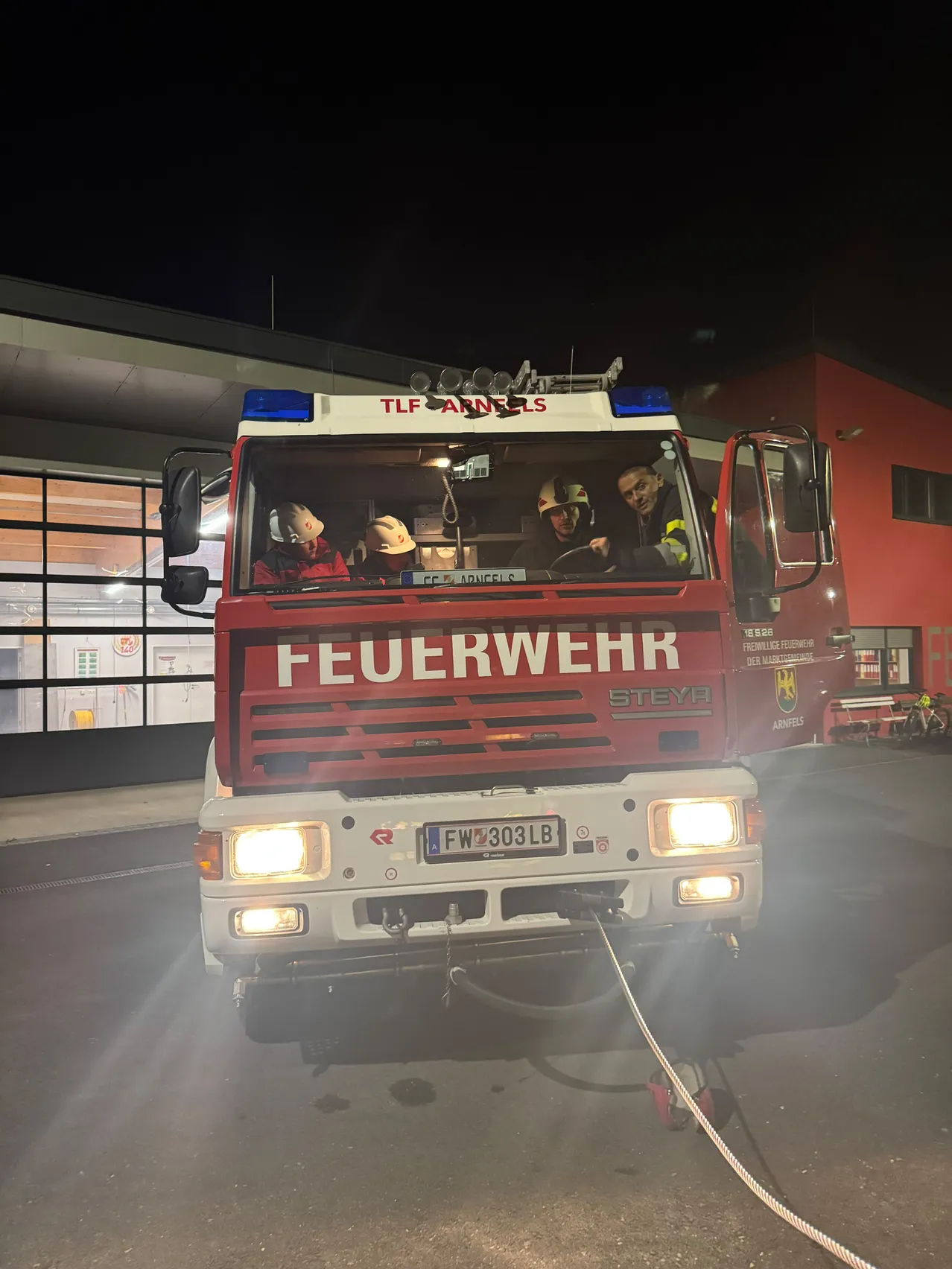 Ein Feuerwehrauto mit dem Wort 'Feuerwehr' darauf ist nachts vor einem Gebäude geparkt.