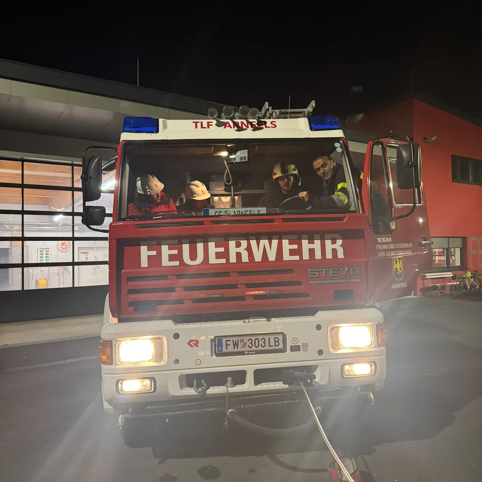 Ein Feuerwehrauto mit dem Wort 'Feuerwehr' darauf ist nachts vor einem Gebäude geparkt.