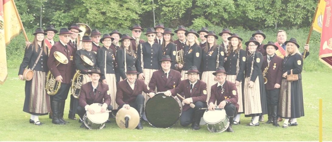 Eine Musikgruppe in traditioneller Kleidung posiert mit Instrumenten und Fahnen für ein Bild. Das Plakat kündigt ein Sommerkonzert des Musikvereins Heimatklange Loipersdorf am 26. Juni 2026 um 19 Uhr im Gasthaus Hauer an.