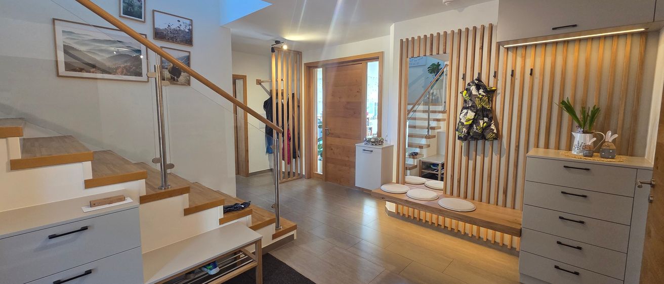 Innenraum eines modernen Hauses mit gefliestem Boden, einer Treppe und einer Holzwand mit Haken für Jacken.