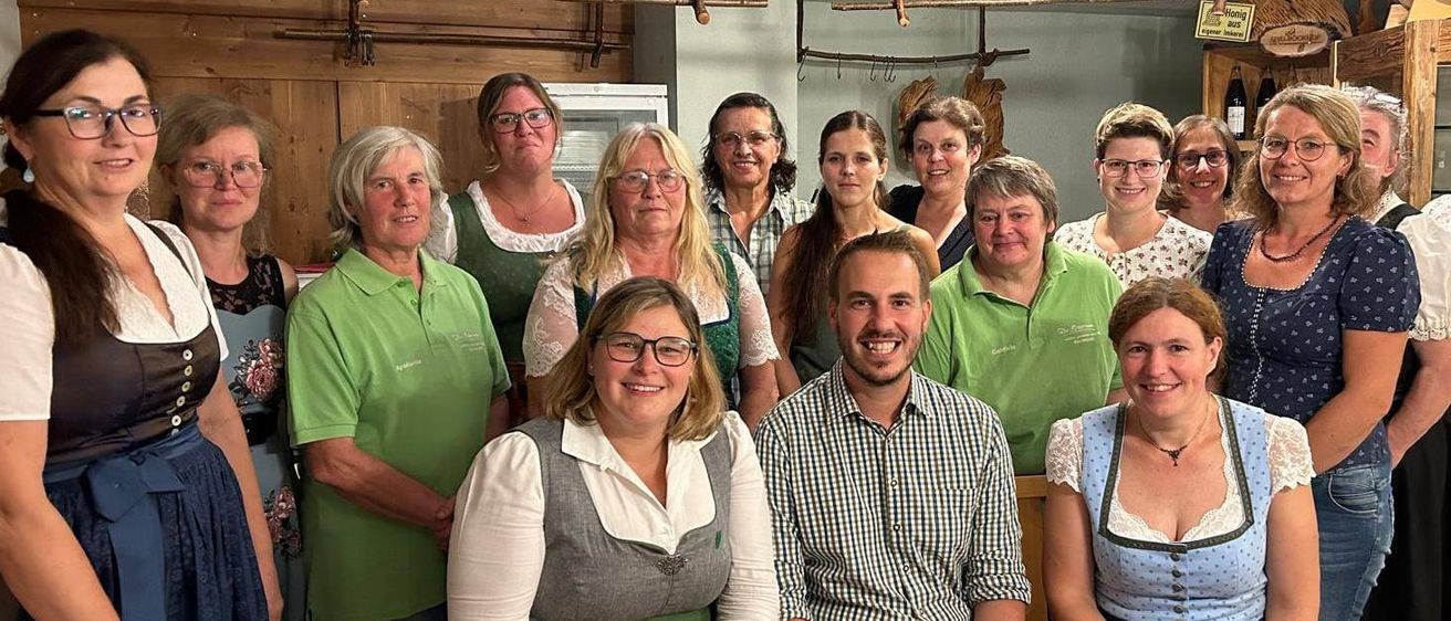 Eine Gruppe von Frauen und Männern in grünen Shirts und traditioneller Kleidung posiert für ein Foto in einem Raum mit Holzwänden.