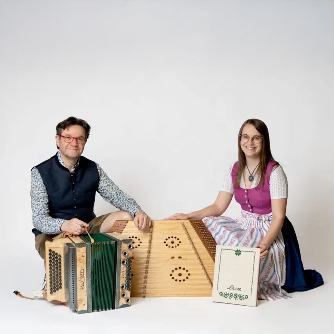 Two individuals pose with traditional accordions and a book, likely musicians in traditional attire.