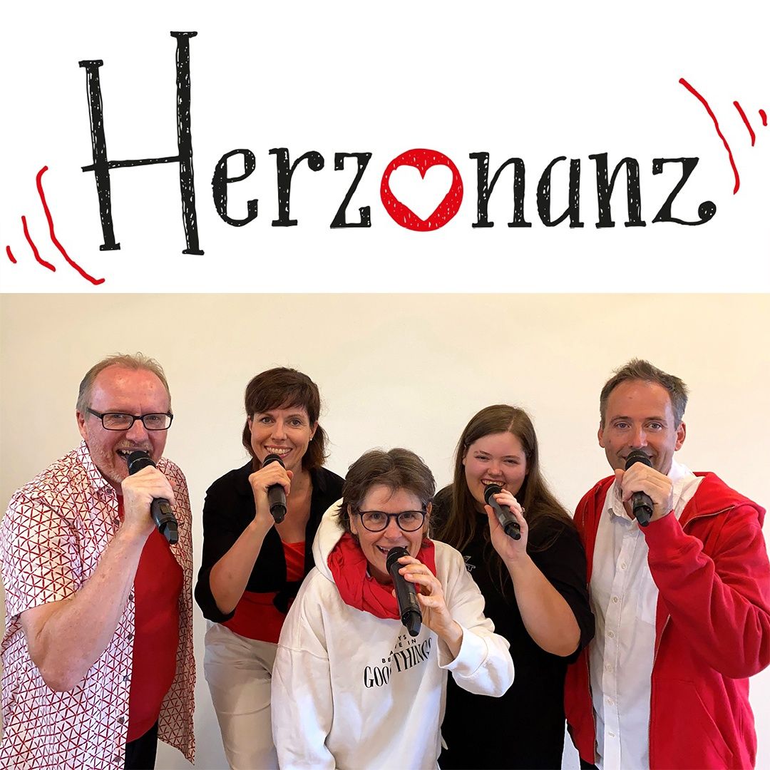 Fünf Personen stehen eng beieinander, jede hält ein Mikrofon, lächelt und posiert für ein Foto mit dem Wort Herzonanz über ihnen.