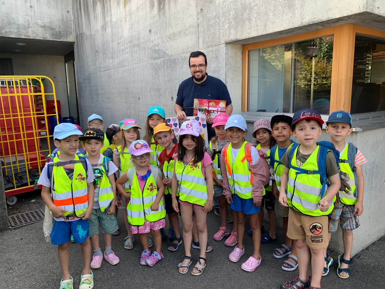 Eine Gruppe von Kindern in Sicherheitswesten steht vor einem Mann, der eine Geschenkbox hält. Sie lächeln und posieren für ein Foto.