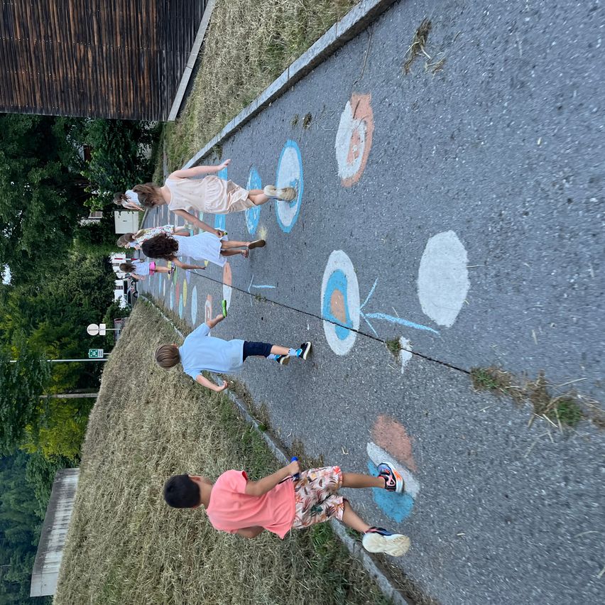 Eine Gruppe von Kindern spielt ein Spiel auf einem Kreidefeld und springt über Linien und trifft Ziele.