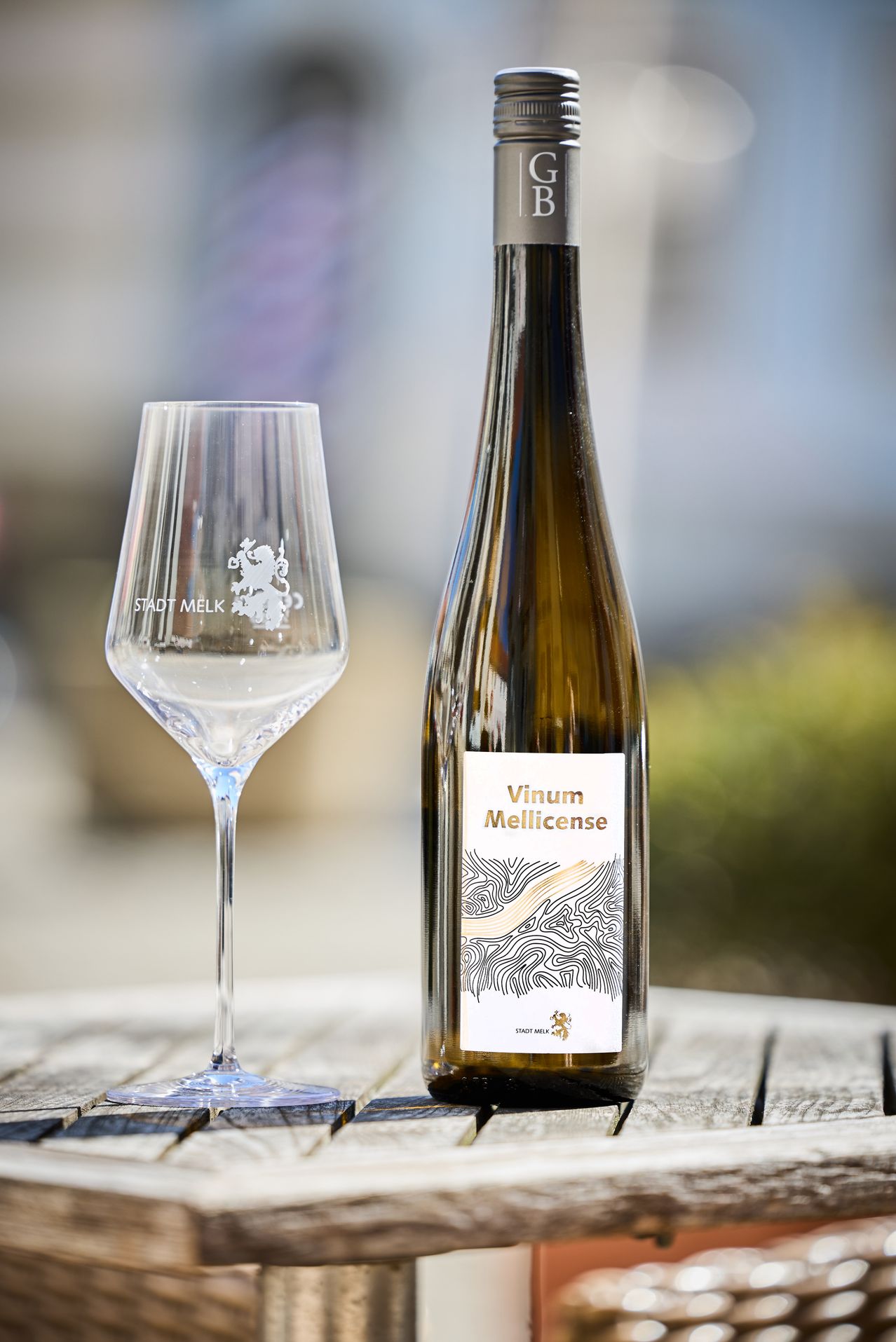 Eine Flasche Vinum Mellicense steht neben einem klaren Weinglas auf einem Holztisch.