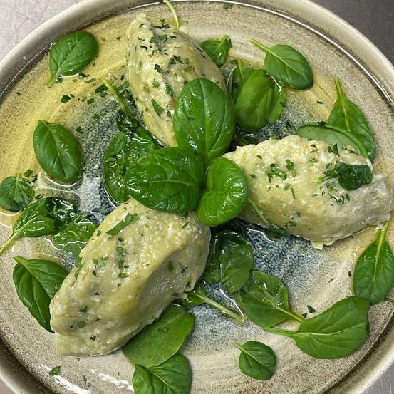 Ein Teller mit vier gefüllten Pasteten, überzogen mit grüner Sauce, garniert mit frischen Basilikumblättern. Die Pasteten sind rund und goldbraun.