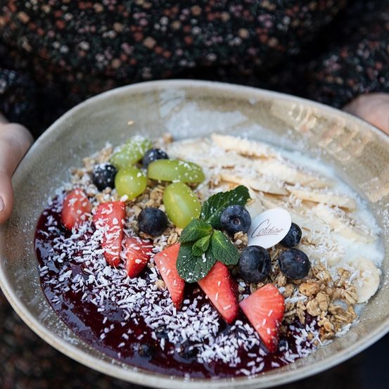 Eine Schüssel mit Müsli, frischen Beeren, Bananen und Kokosflocken, überzogen mit einer Beerensauce und Minzblättern.