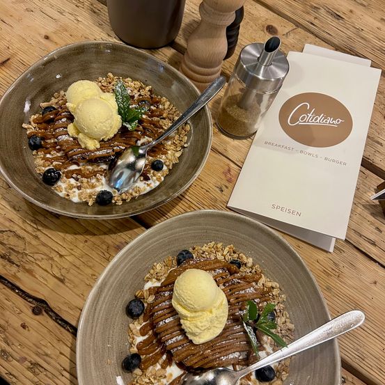 Zwei Schüsseln eines Desserts mit Eiscreme und Granola, begleitet von einem Salzstreuer und einem Menükarten von Cotidiana.