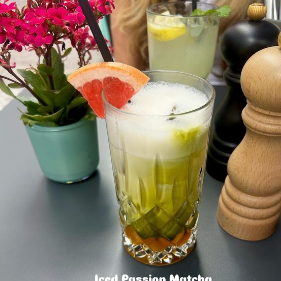 Ein grünes Getränk mit einer Orangenscheibe obenauf steht auf einem Tisch mit Blumen und Salz- und Pfefferstreuern.