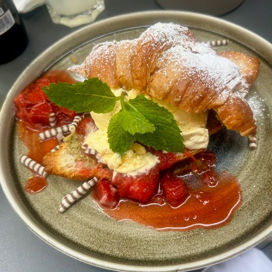 Ein Teller zeigt ein Croissant gefüllt mit Erdbeerscheiben, Eiscreme und Minzblättern, überzogen mit einer süßen Soße.