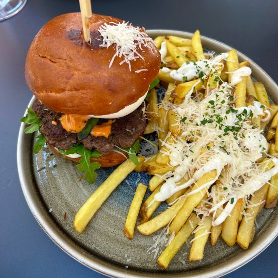 Ein Teller enthält einen Cheeseburger mit Salat und Käse, begleitet von einer Portion Pommes Frites, die mit Käse und Kräutern überzogen sind.