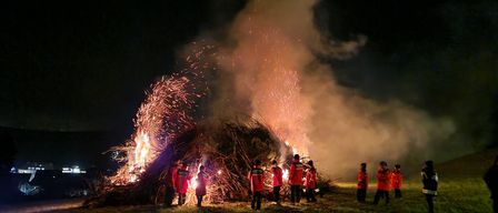 In der Nacht stehen eine Gruppe von Menschen in roten Jacken um ein Lagerfeuer herum und halten brennende Funkenspäne in der Hand.