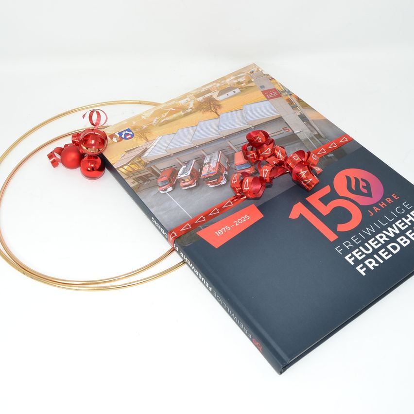 Ein Buch mit dem Titel '150 Jahre Freiwillige Feuerwehr Friedberg' mit roten Ornamenten auf einem goldenen Ring auf weißem Hintergrund.