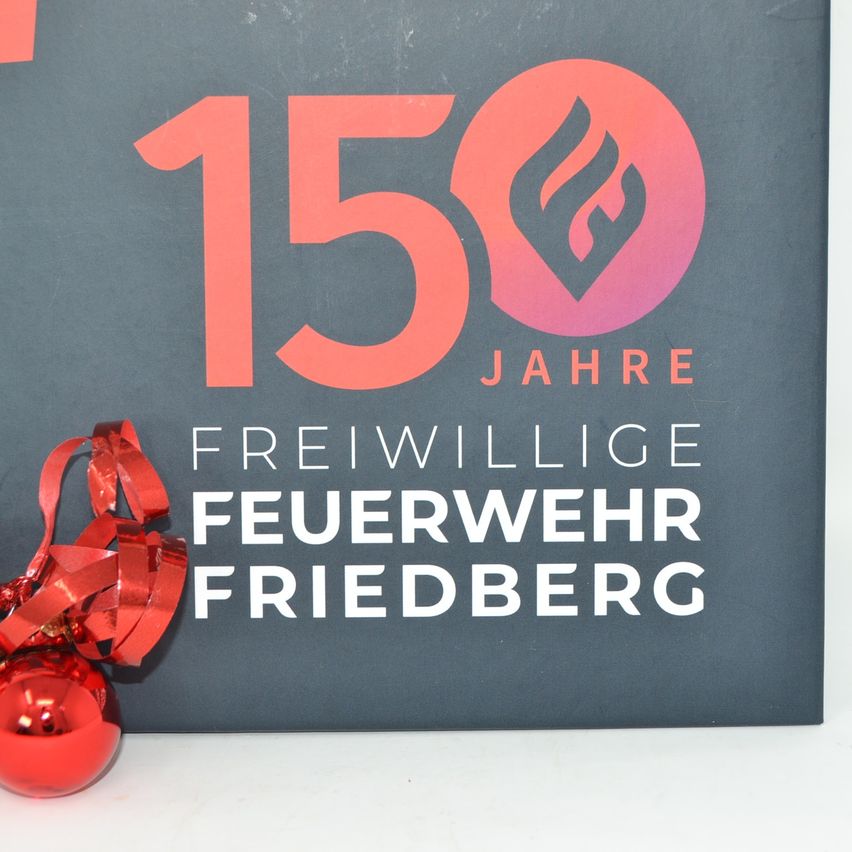 Ein Schild zur Feier der 150 Jahre der Freiwilligen Feuerwehr Friedberg, mit einem roten Band und einer Dekoration.