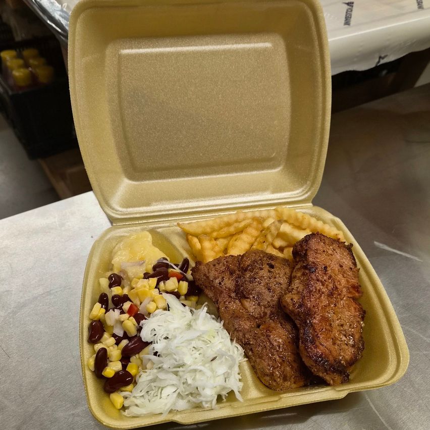 A yellow cardboard container with a meal inside, featuring grilled steak, French fries, corn, beans, and sauerkraut.