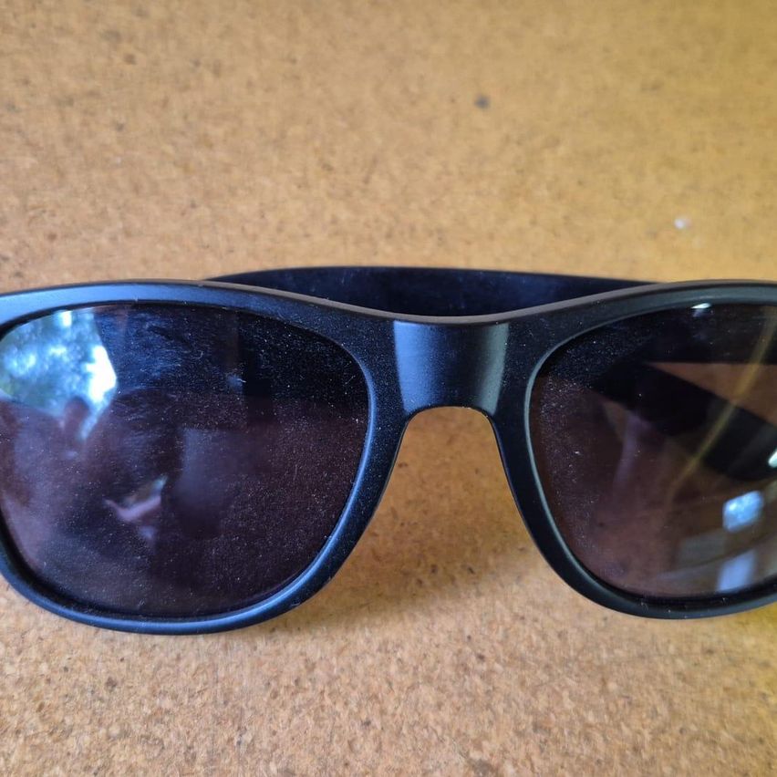 A pair of black sunglasses with reflective lenses on a brown surface.