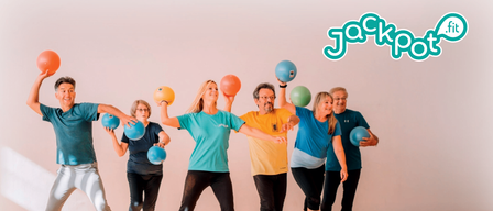 Eine Gruppe von Erwachsenen nimmt an einem Fitnesskurs teil, hält blaue Bälle und trägt Trainingskleidung. Das Plakat im Hintergrund bewirbt ein Gesundheitssportprogramm in Eichgraben und hebt Motivation, Kraft und Ausdauertraining für Erwachsene hervor.
