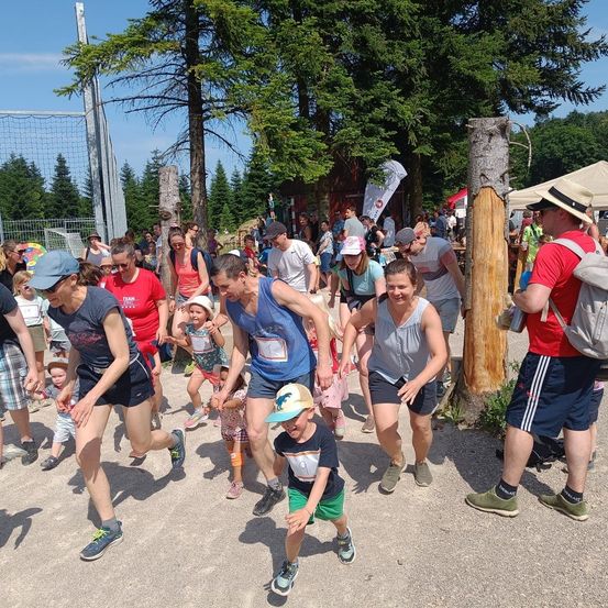 Eine Gruppe von Menschen, einschließlich Erwachsener und Kinder, läuft in einem Rennen in einem Park. Sie tragen Mützen und Turnschuhe. Bäume und ein Netzzaun sind in der Gegend.