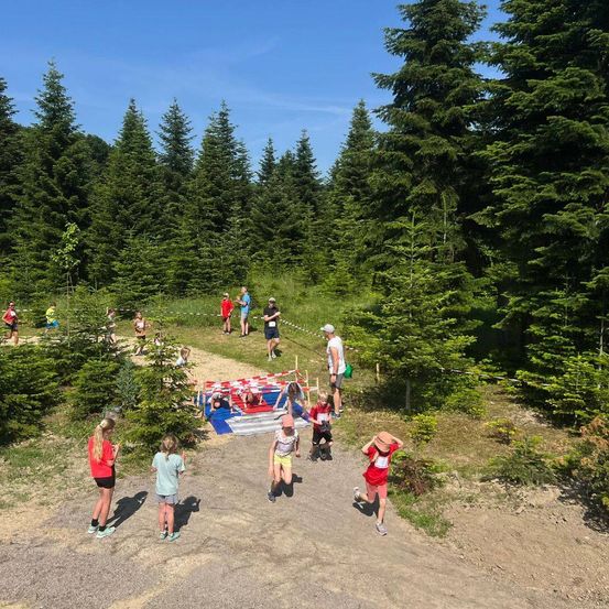 Eine Gruppe von Kindern läuft ein Rennen im Wald. Einige sind auf der Rennstrecke, andere beobachten. Bäume und Büsche sind um sie herum.