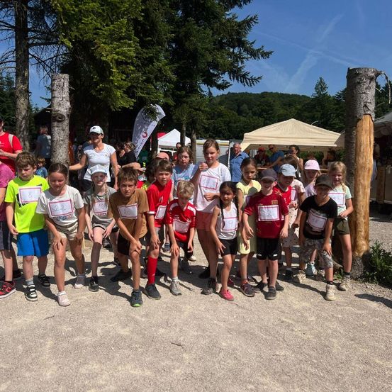 Eine Gruppe von Kindern in einer Reihe mit Nummern auf ihren Trikots. Sie sind draußen an einem sonnigen Tag.