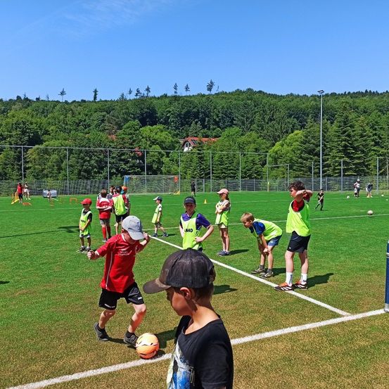 Ein Fußballtraining mit Kindern in grünen Westen auf einem Rasenfeld bei blauem Himmel.