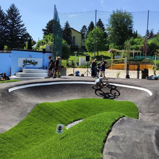 Ein Radfahrer fährt auf einem Rasenstück mit weißem Rand um die Bahn. Zuschauer stehen an der Seite.