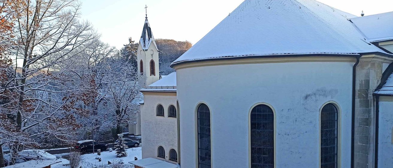 Eine schneebedeckte Kirche mit einem Turm und einem schneebedeckten Dach, umgeben von schneebedeckten Bäumen.