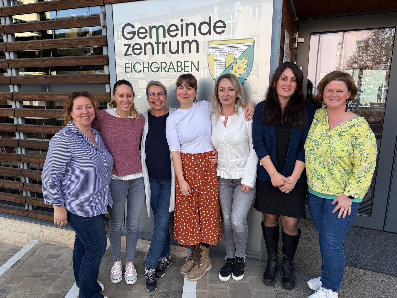 Eine Gruppe von Frauen in Freizeitkleidung steht vor dem Schild des Gemeinde Zentrum Eichgraben. Sie lächeln und scheinen für ein Foto zu posieren.